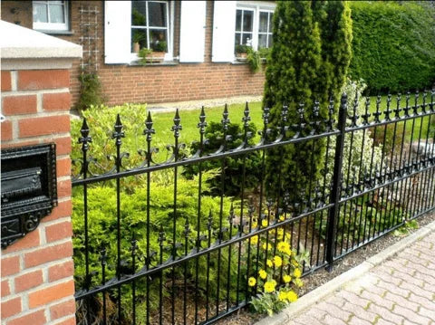 Elegante recinzione in ferro battuto nero davanti a una casa con giardino fiorito e pilastro in mattoni con cassetta delle lettere.